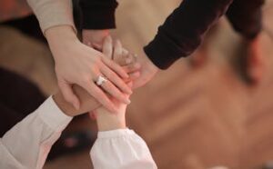 Top view of faceless friends in different clothes stacking hands together while standing on wooden floor indoor on sunny day